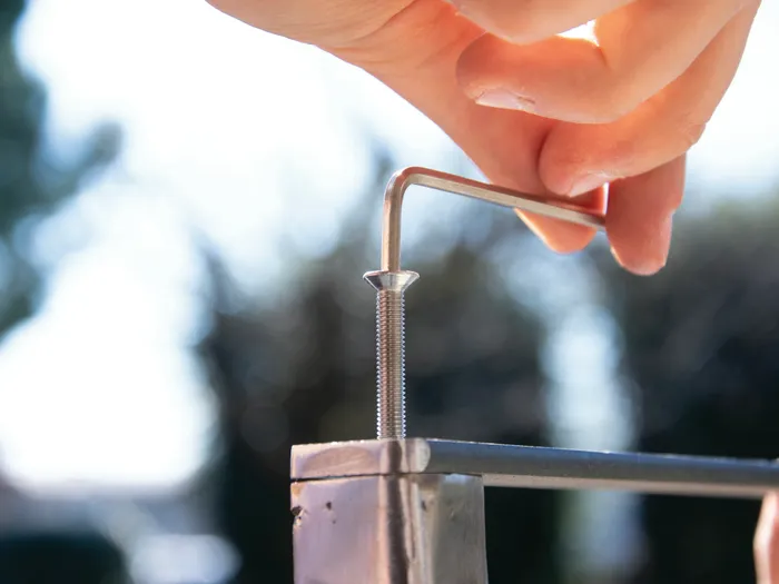 A hand tightening a stainless steel screw at the top of a square steel fence post with a hexagon key, the rail already fixed in place